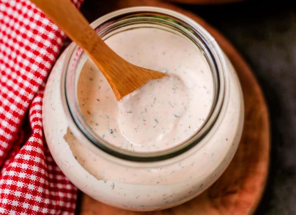 A jar of ranch dressing with a wooden spoon.