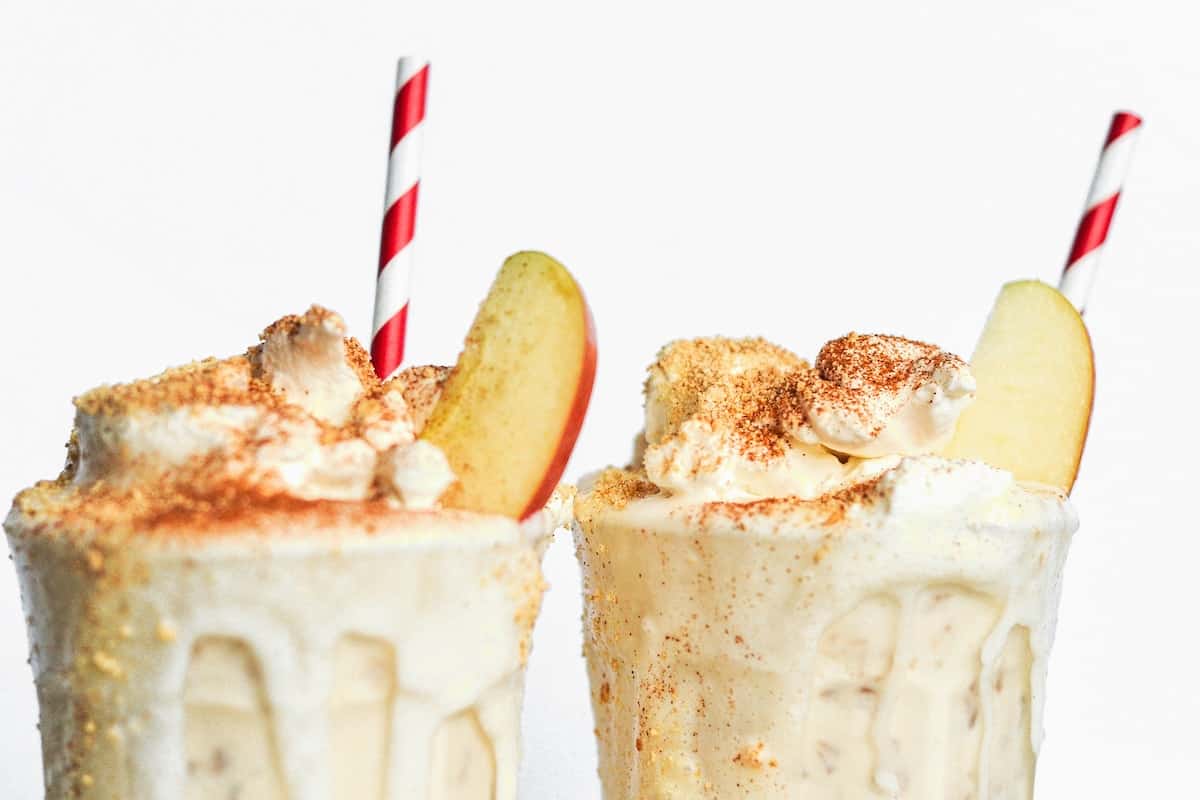 Two milkshakes with whipped cream and apple slices – the perfect indulgence for those craving delicious apple recipes.