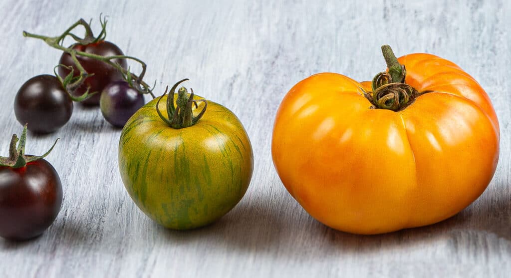 A group of heirloom tomatoes on a wooden surface.