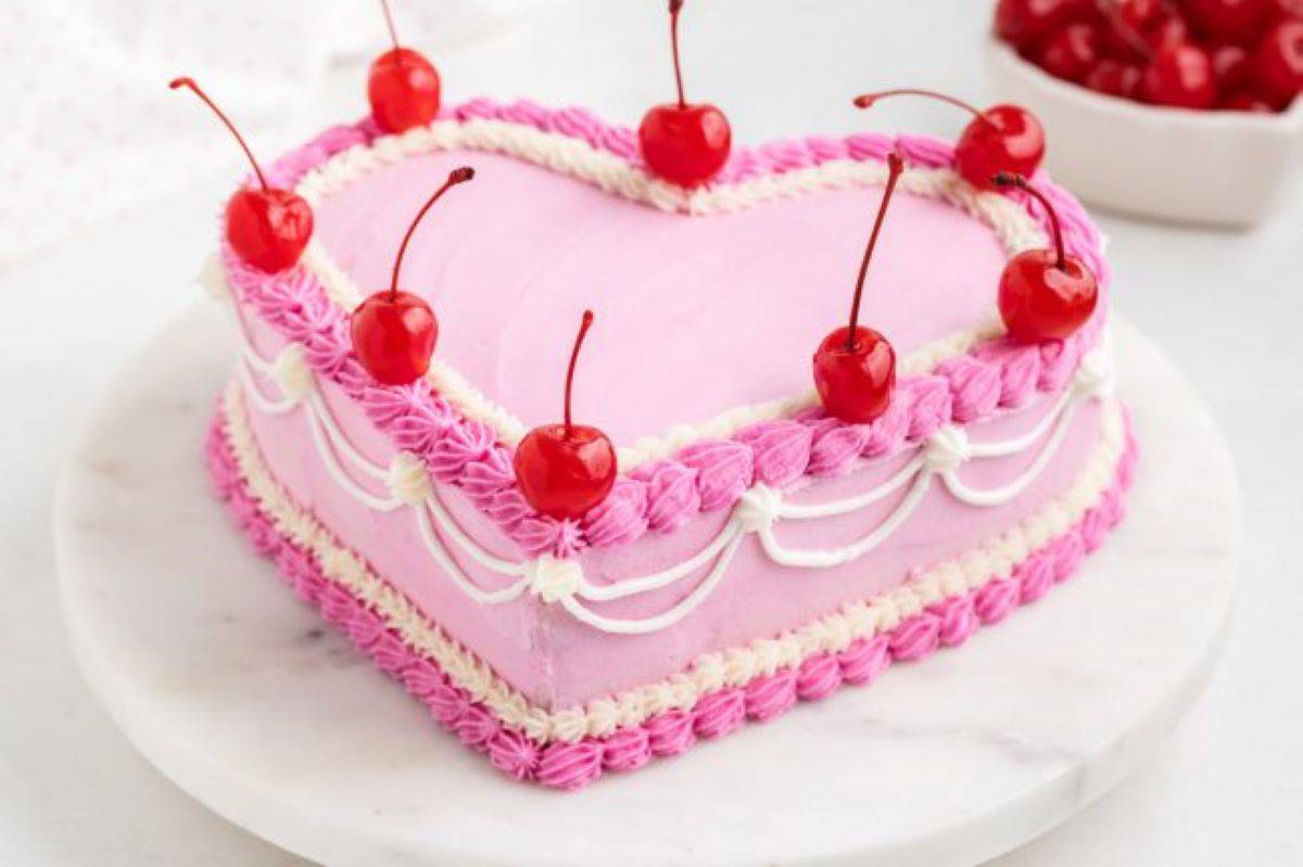 A pink and white vintage heart cake with marschino cherries on top.