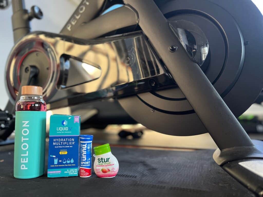 A spinning bike with a bottle of sunscreen and other items, including the best water enhancers, on it.