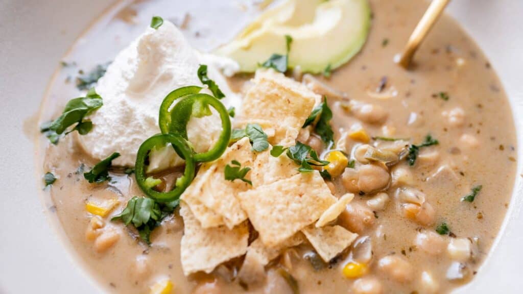 A bowl of mexican bean soup with sour cream and avocado.