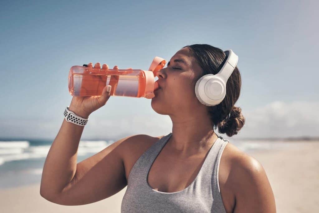 A woman enjoying her favorite water enhancer while listening to music on the beach.