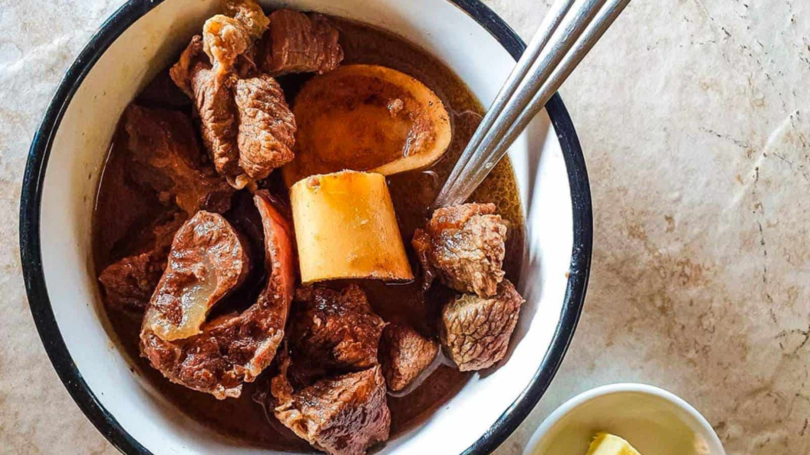 A bowl of beef stew with a spoon and marrow bones.
