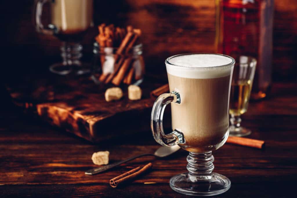 A glass of latte with cinnamon sticks on a wooden table.