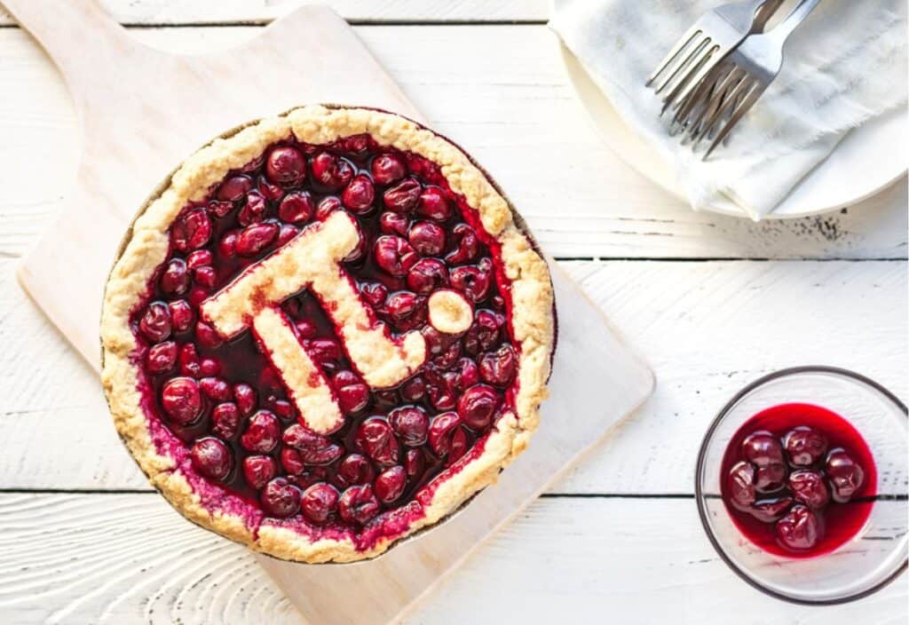 Pi pie with cherries on a wooden cutting board.