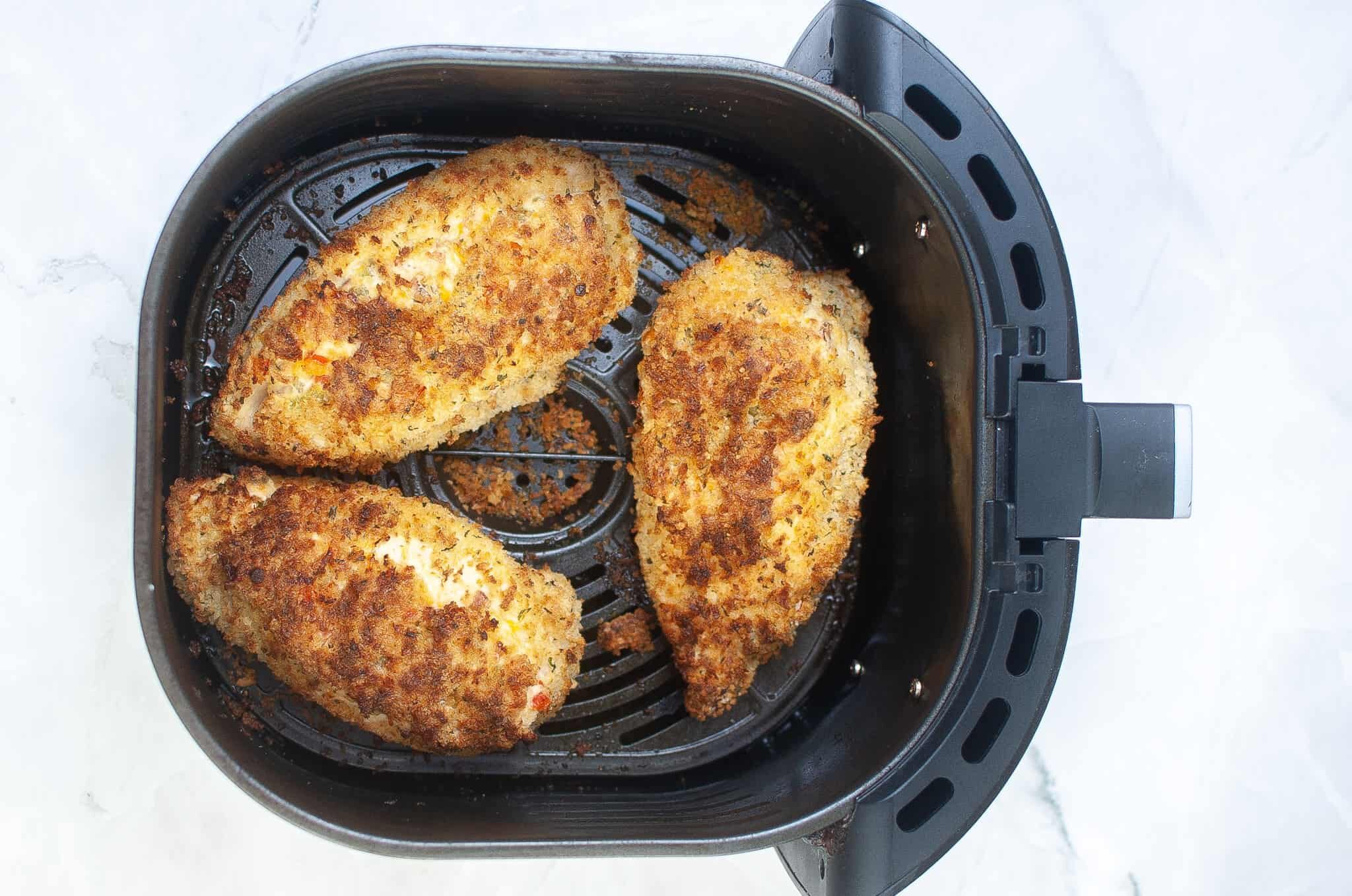An air fryer basket with stuffed chicken breasts.