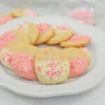 A plate of pink and white cookies with sprinkles on it.