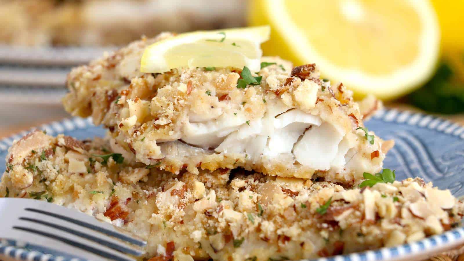 A plate of almond-crusted walleye or pickerel fish fillets with a fork and lemon.