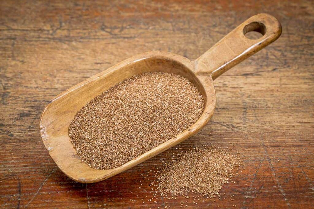 Teff grains in a wooden scoop on a wooden table.