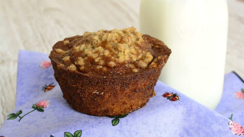 A muffin sitting on a napkin next to a glass of milk.