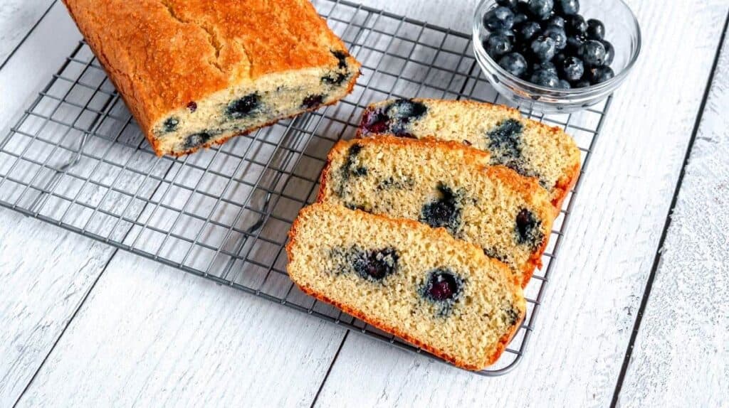 Blueberry bread on a cooling rack with blueberries.