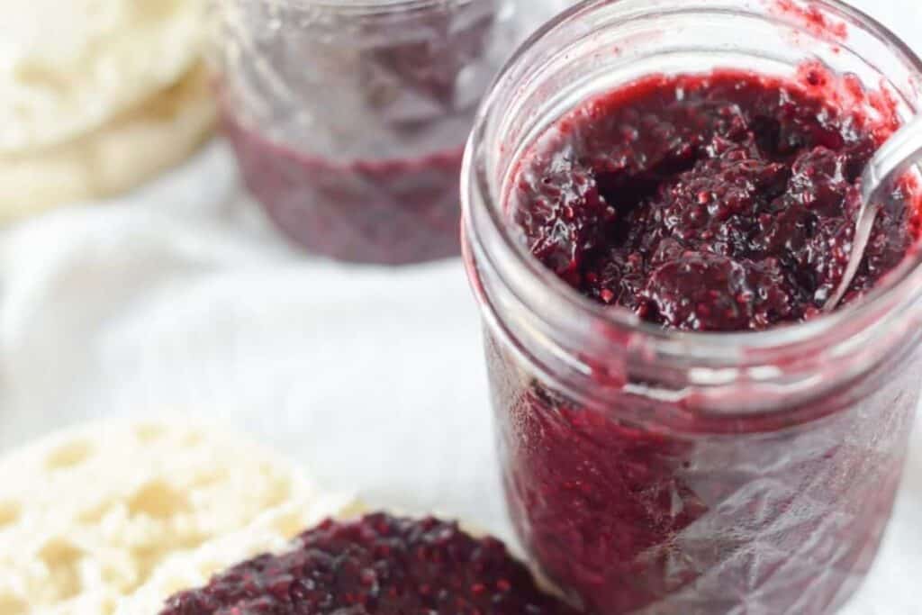 A jar of blackberry jam with a spoon next to it.