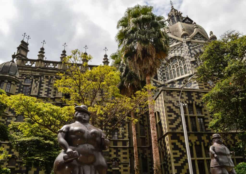 A pair of statues standing in front of a grand building, located in Medellín.
