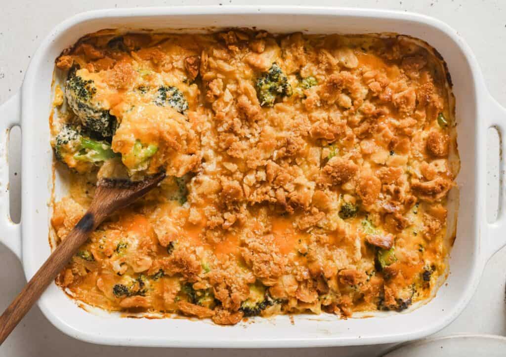 Broccoli casserole in a white dish with a wooden spoon.