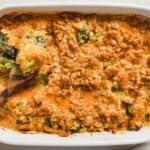 Broccoli casserole in a white dish with a wooden spoon.