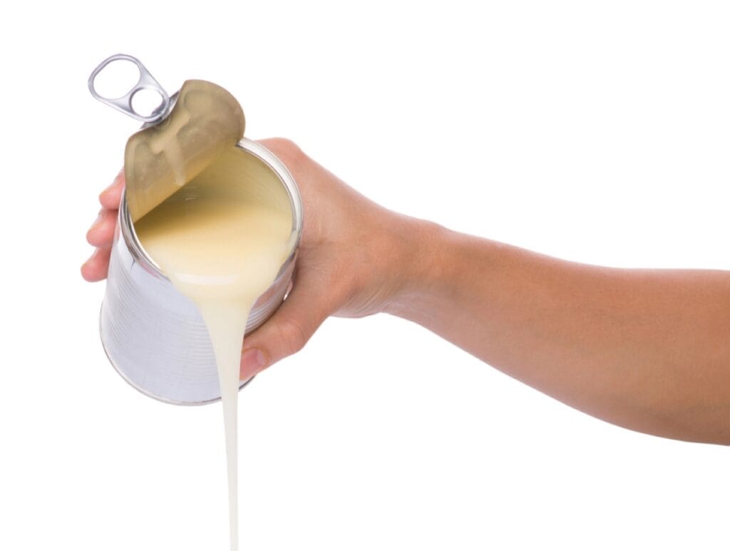 A person pouring sweetened condensed milk from a can.