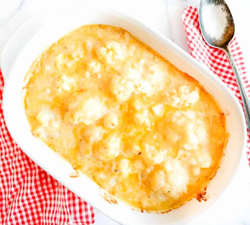 Cheesy cauliflower casserole in a white dish with a spoon.
