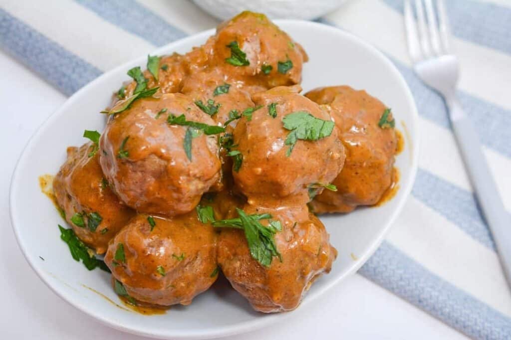 Meatballs in a white bowl with sauce and a fork.