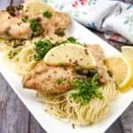 Two chicken piccata on a white plate with parsley and lemon wedges.