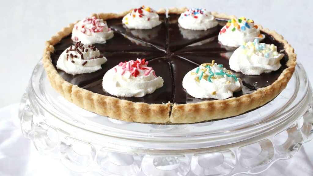 A chocolate tart with whipped cream and sprinkles on top.
