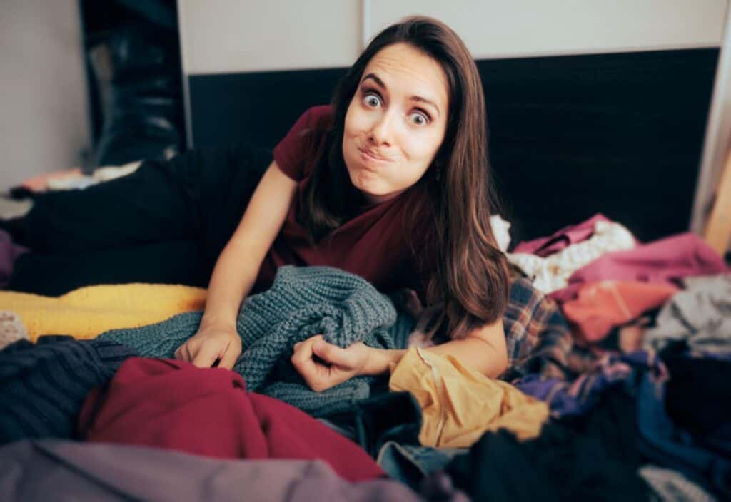 A woman lays on top of a clutter of clothes.