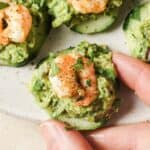 A person holding a cucumber with shrimp and guacamole.