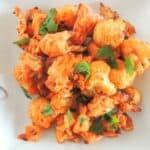 A plate of baked spicy cauliflower bites with red sauce next to it.