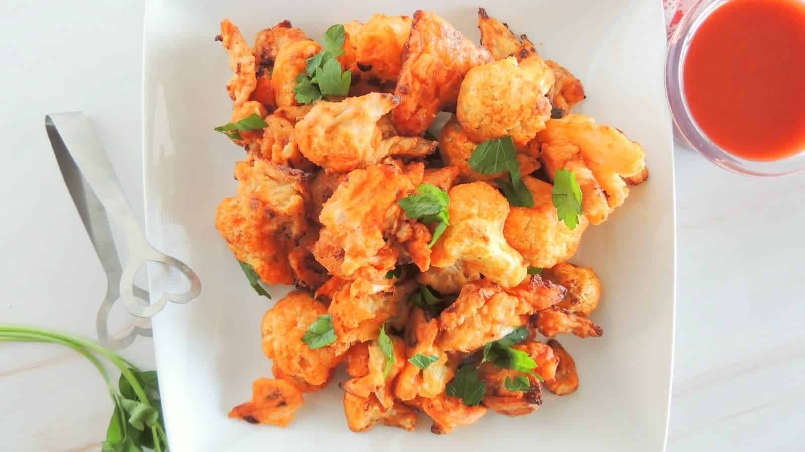 A plate of baked spicy cauliflower bites with red sauce next to it.