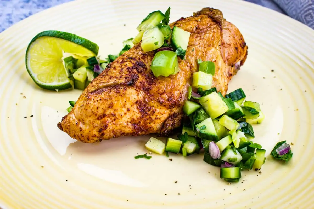 A plate with chicken and cucumbers salsa on it.