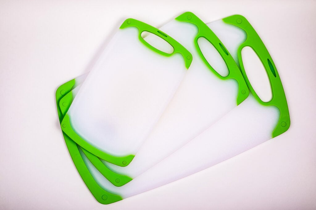 Three green trimmed plastic cutting boards on a white surface.