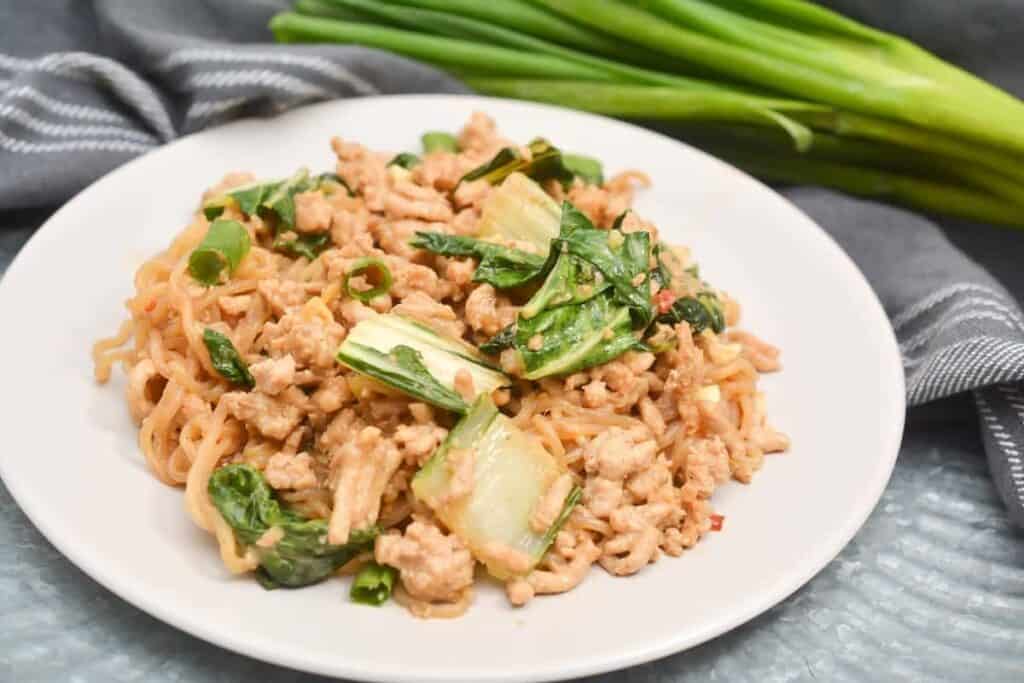 A plate of asian fried rice with chicken and greens.