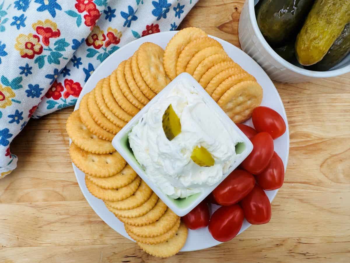 Pickle dip with crackers and tomatoes on a plate.