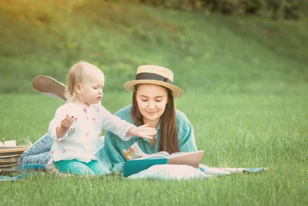 A mother and child reading a book in the grass.