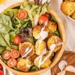 A bowl of falafel with tomatoes, lettuce, and dressing.