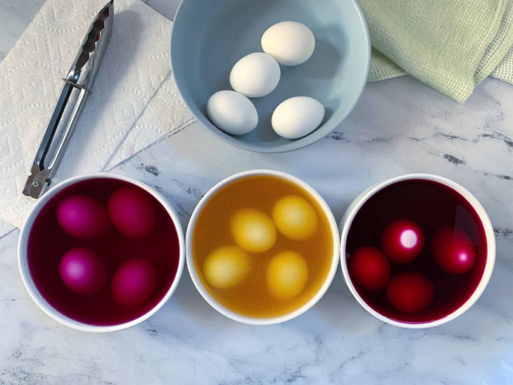 Three bowls of eggs with different colors in them.