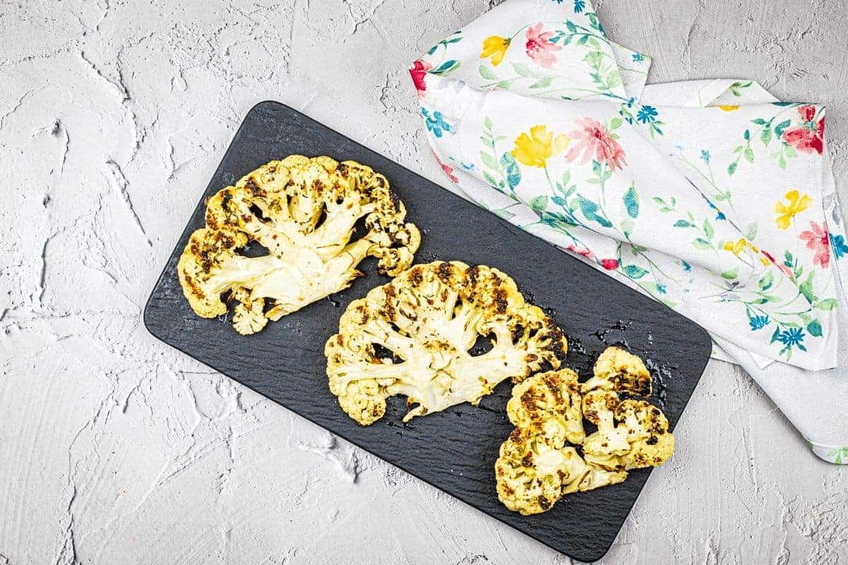 Three pieces of grilled cauliflower steaks on a black plate.