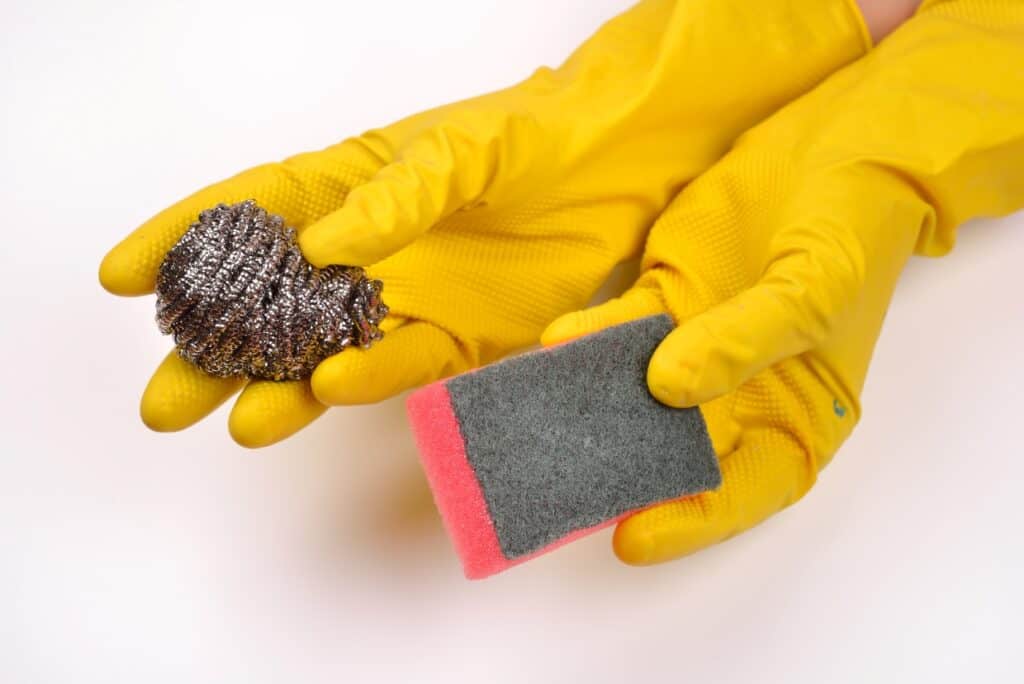 A pair of yellow gloves holding a sponge and steel wool.