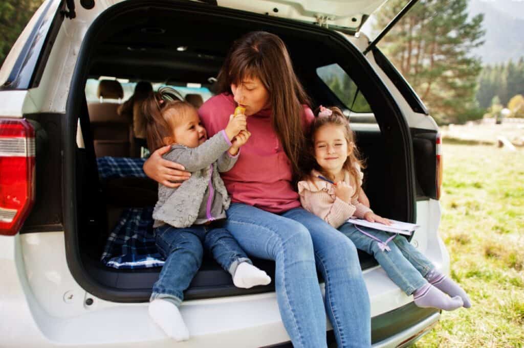 A woman and her children are sitting in the trunk of a car.