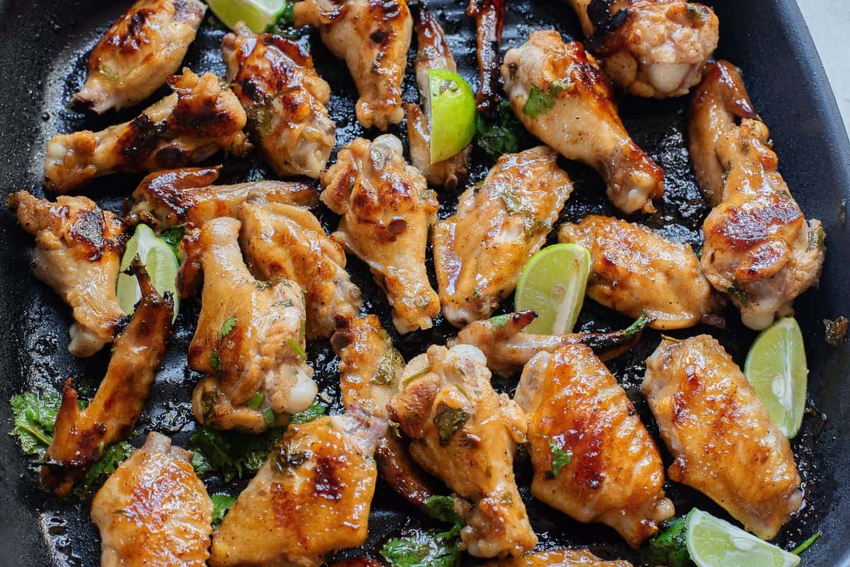 Gluten-free chicken wings in honey garlic sauce on a grill pan with cilantro and lime on them.