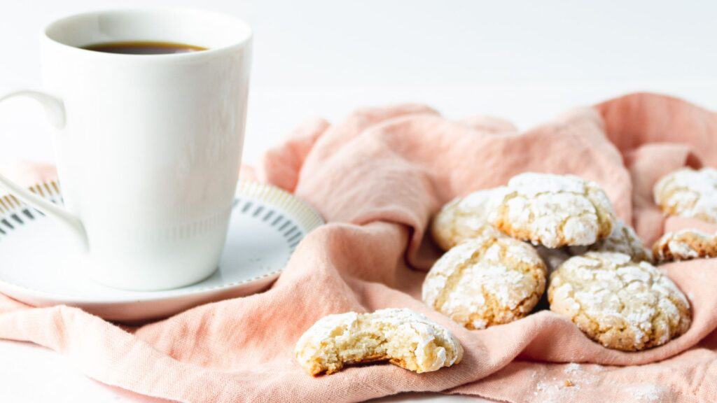 A cup of coffee and a cup of powdered sugar cookies.