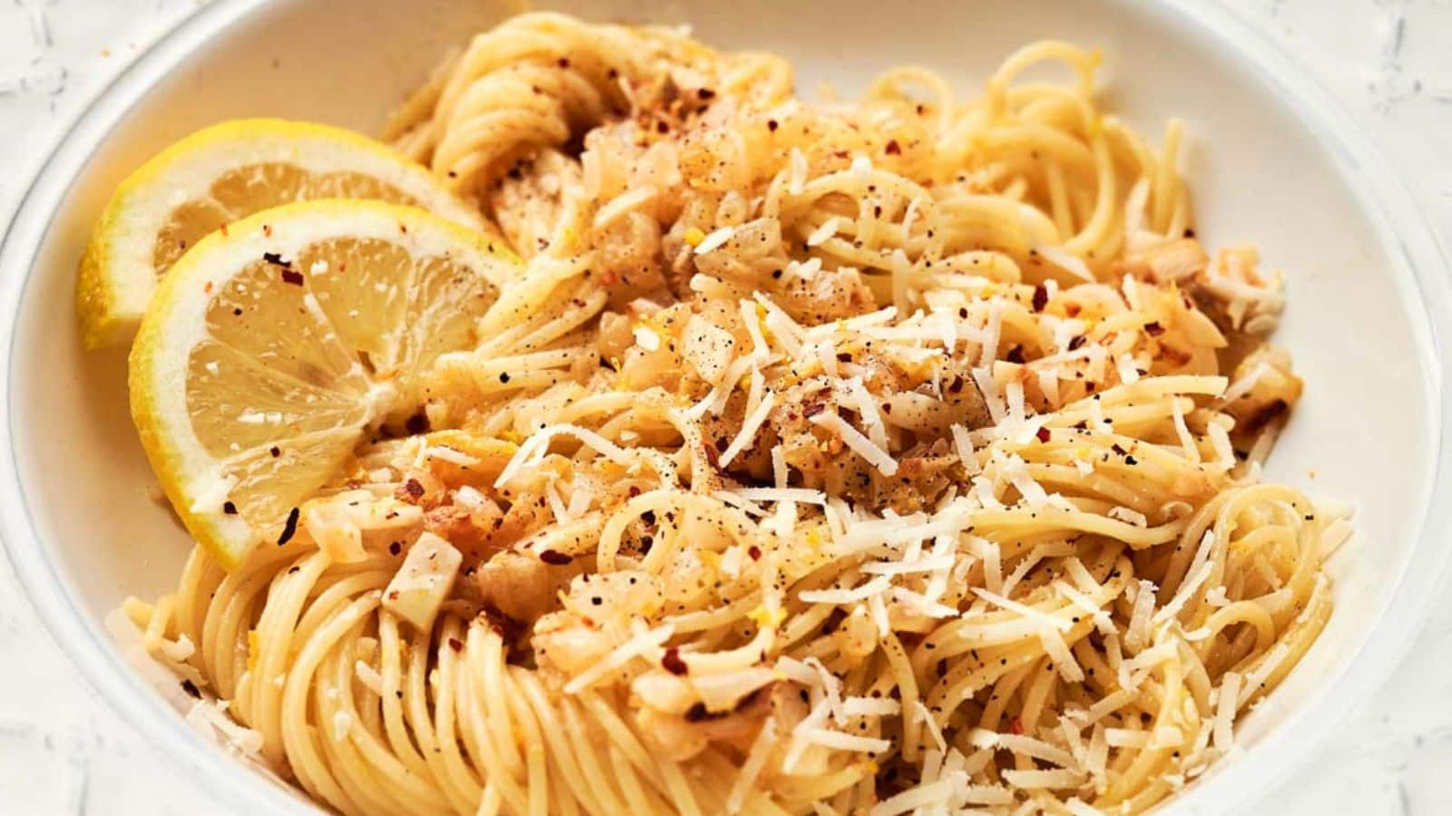 A bowl of pasta with lemon slices and parmesan cheese.