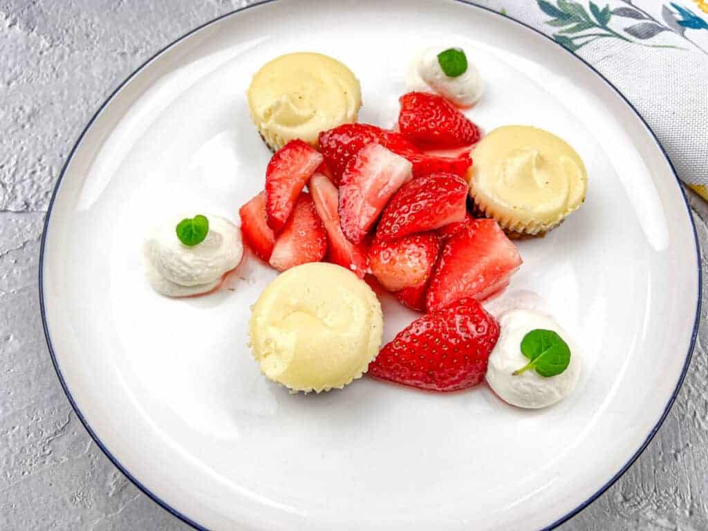 A white plate with strawberries and mini biscoff cheesecakes.
