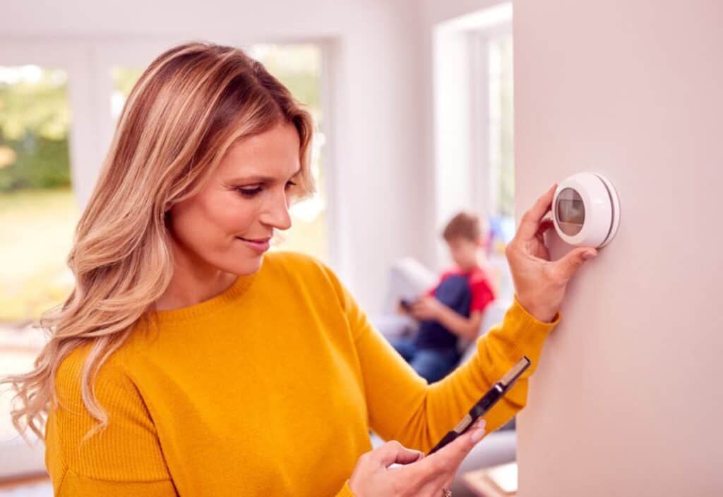 Learn how to save on your heating bill with a smart thermostat used by a woman in her home.