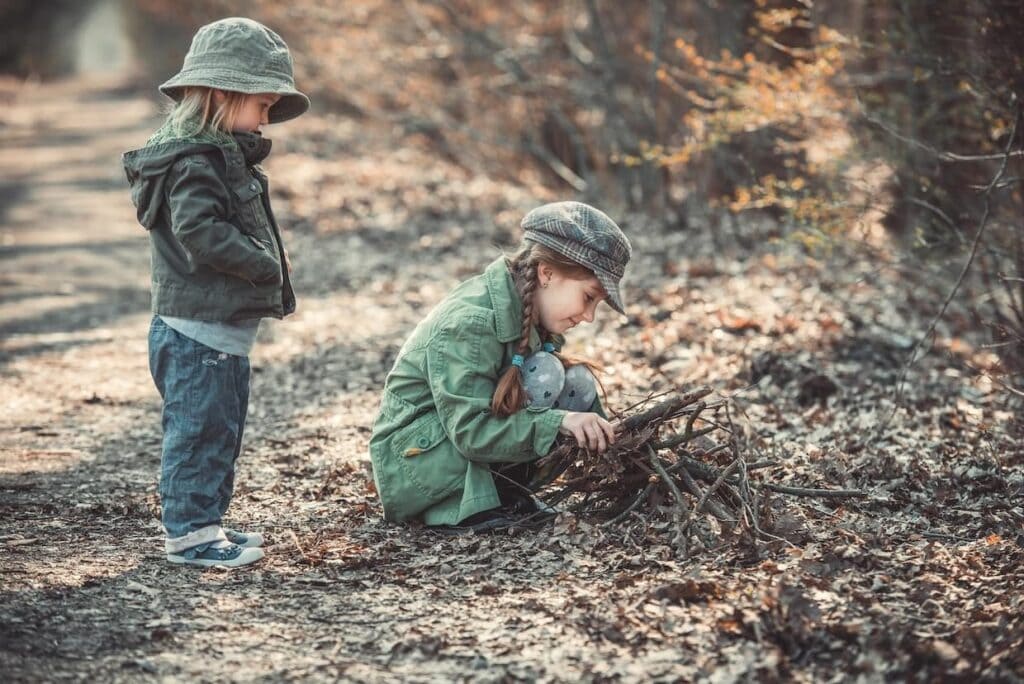 Two children playing with sticks in the woods.