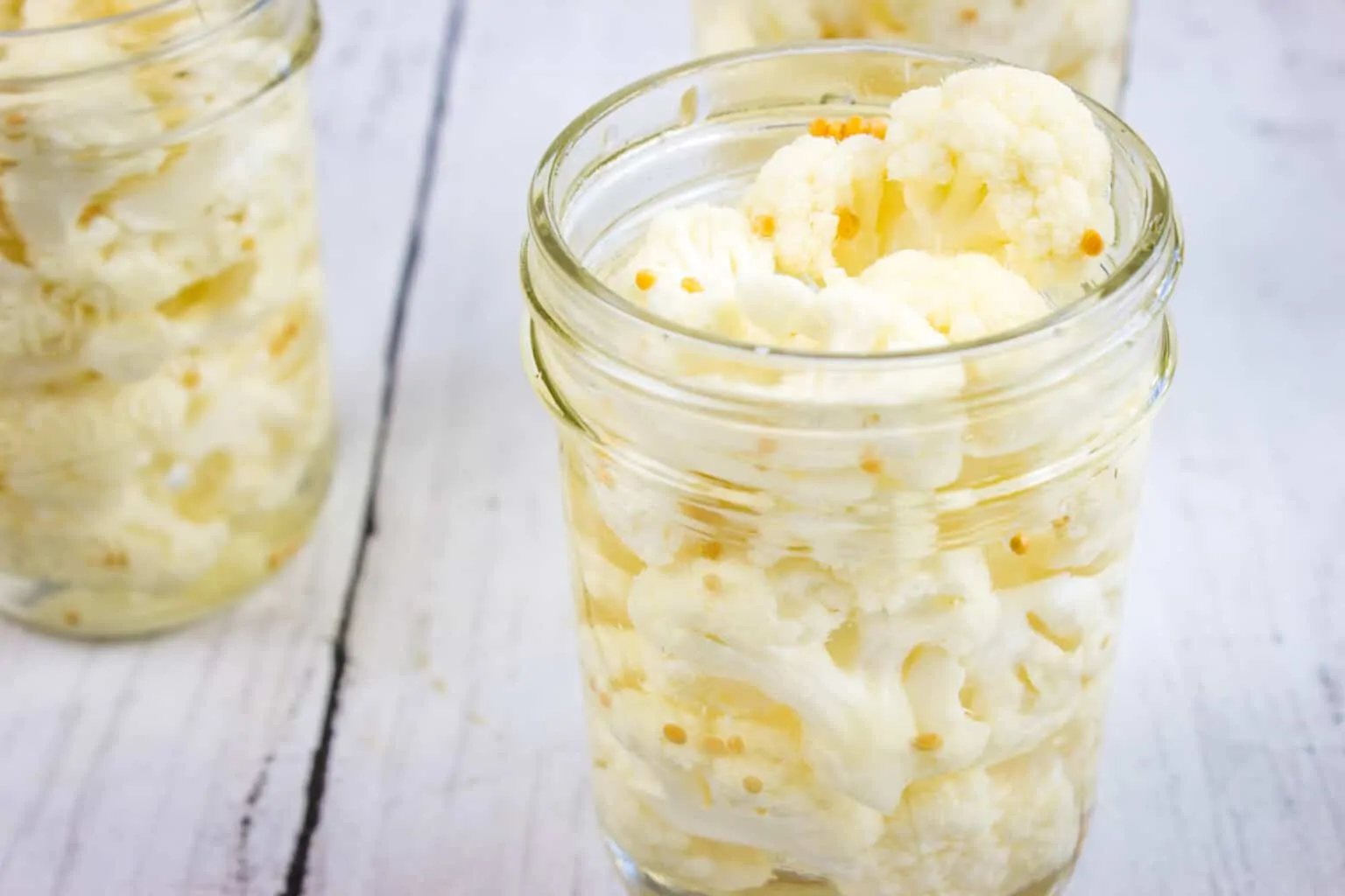 Pickled cauliflower in jars on a wooden table.