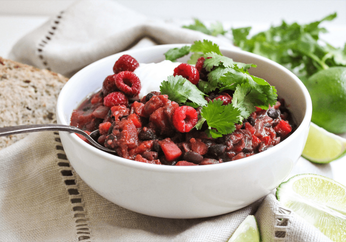 Black bean chili with raspberries topped with cilantro and yogurt in a white bowl.