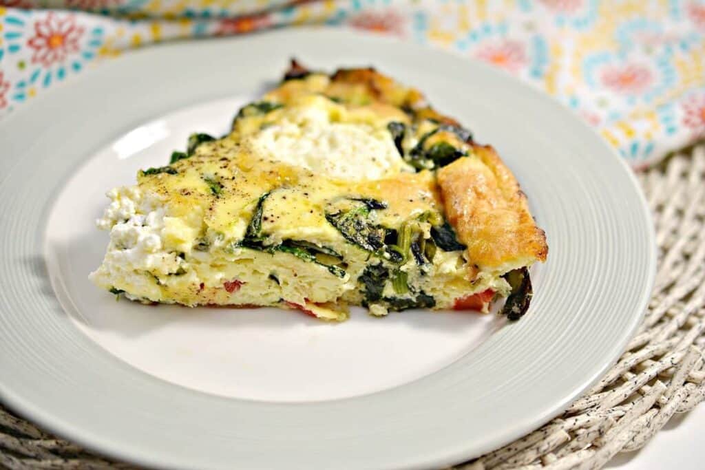 A slice of quiche with spinach and cheese on a plate.