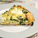 A slice of quiche with spinach and cheese on a plate.