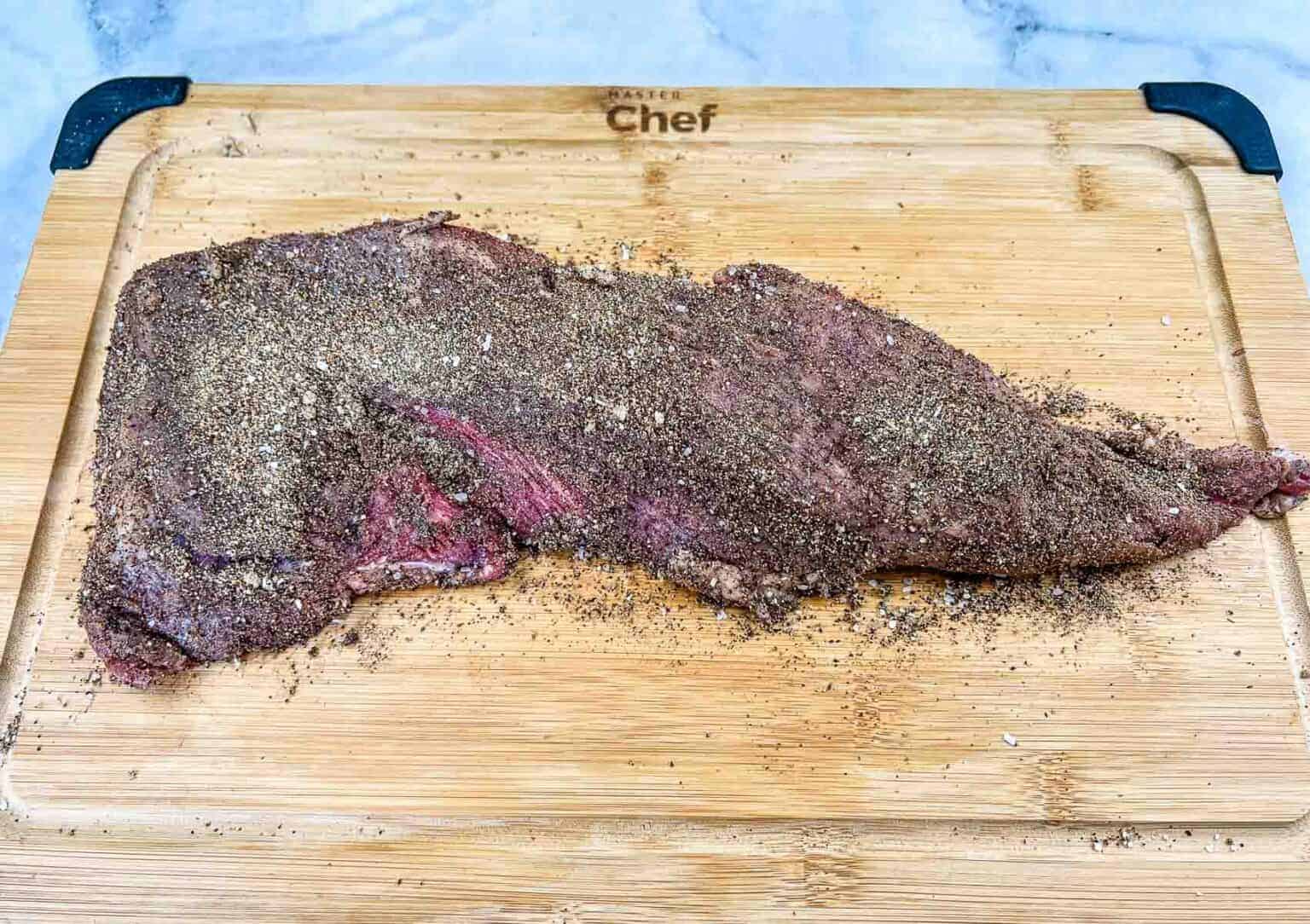 A piece of steak on a cutting board with rub on it.